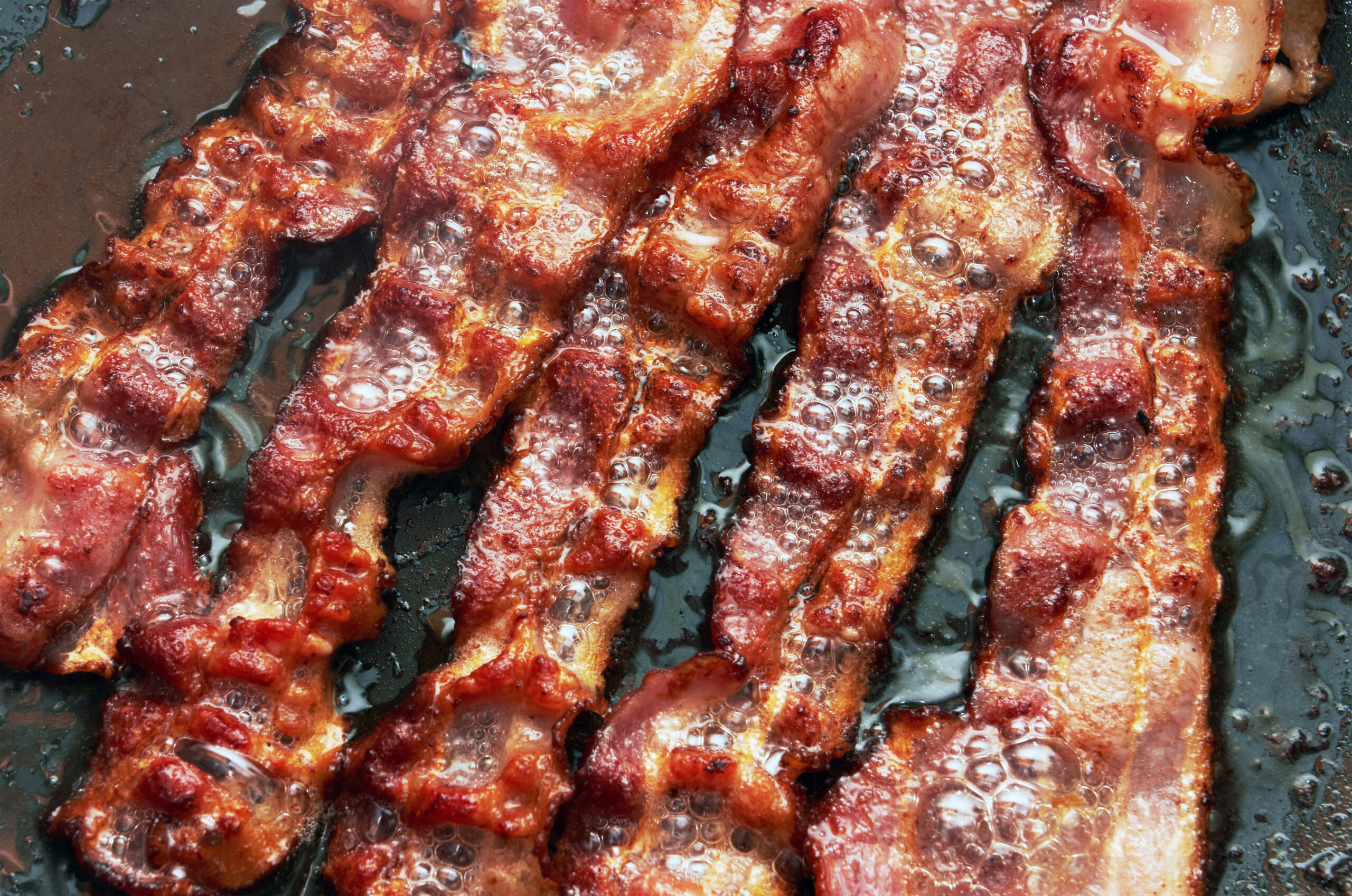 Bacon slice being cooked in frying pan. Close up.