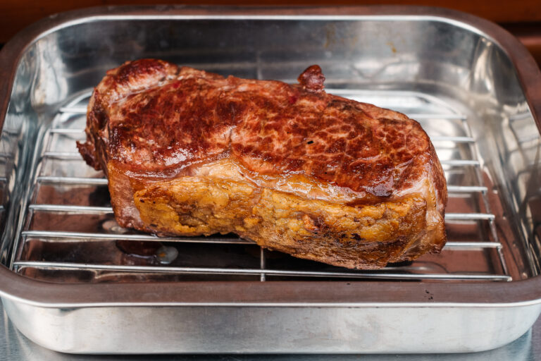 Rumpsteak liegt auf einem Rost und rastet in einem Aluminiumbräter