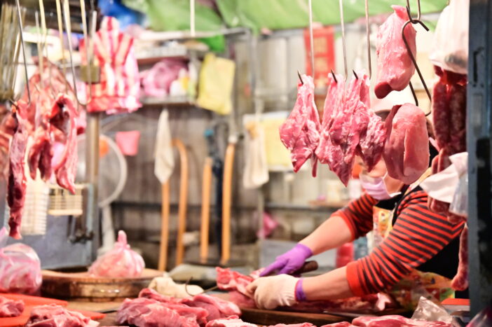 A close-up at a pork stall in the market, where the vendor is handling pork, with other pork products displayed on shelves.