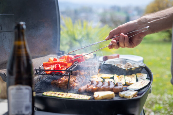 Close up of sausages, steak, cheese and vegetables on gas grill. Summer time, outdoors.