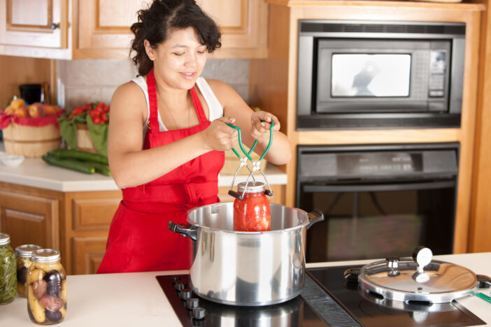 A waist up image of a mixed race (Caucasian, Asian, Pacific Islander) young adult woman canning homegrown fruits and vegetables.