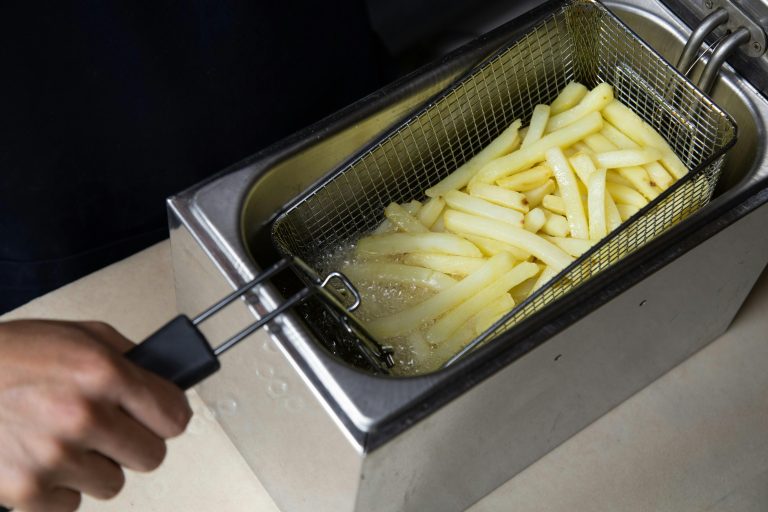 Photo of a person s hand deep frying french fries