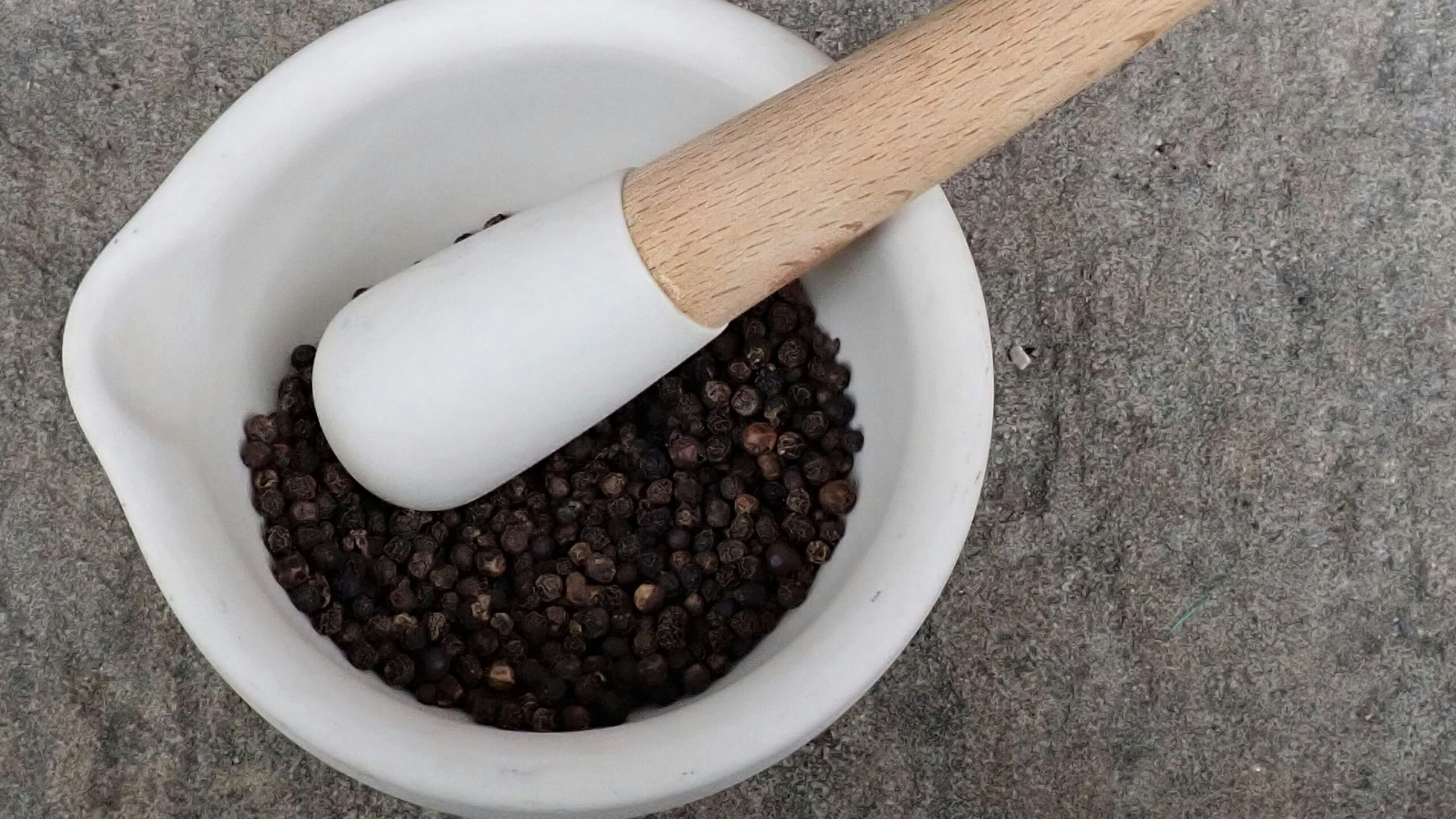 Black Peppercorns, Pestle and Mortar on Stone Surface.