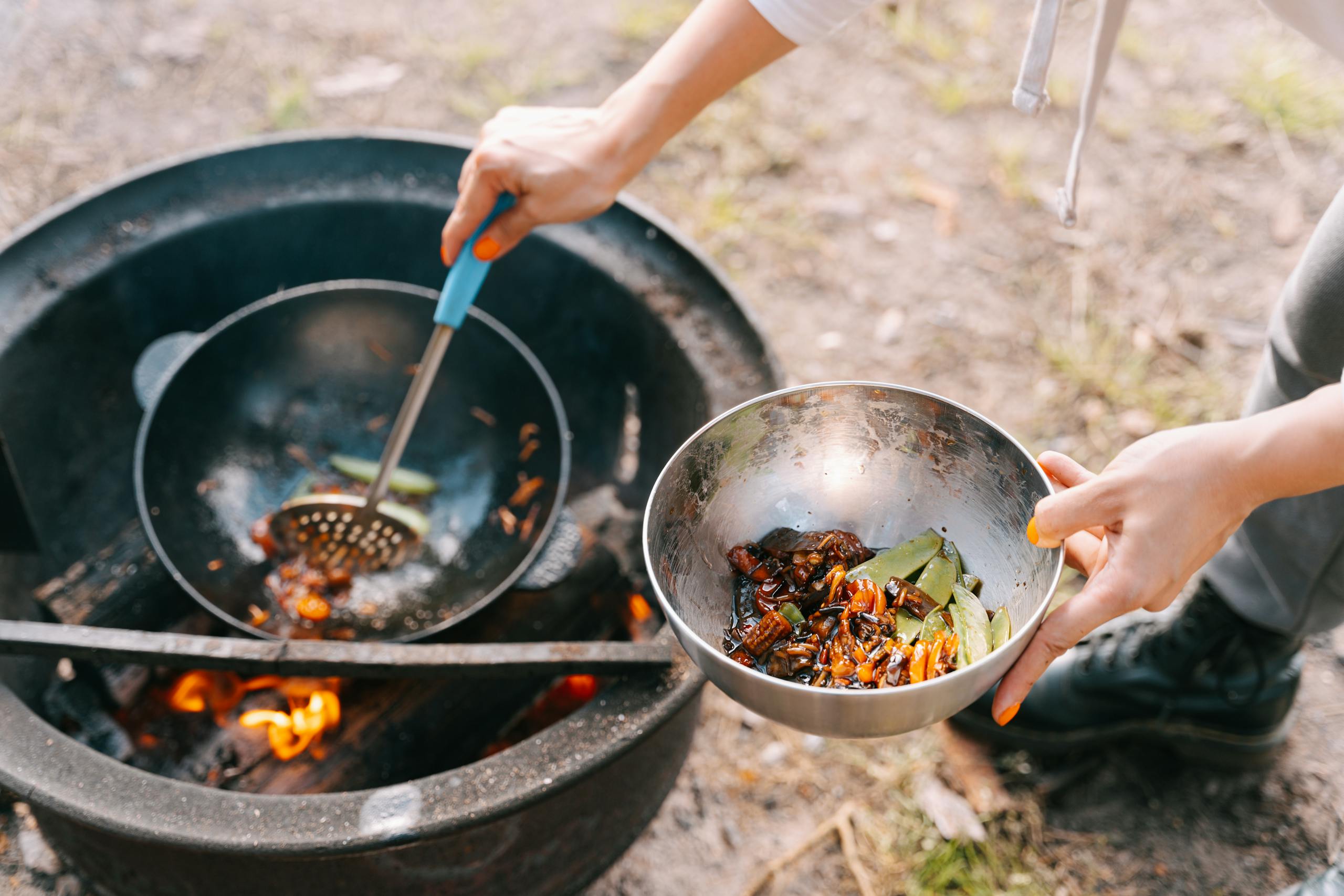 Close-up of Woman Putting Food from a Pan over the Fire into a Bowl