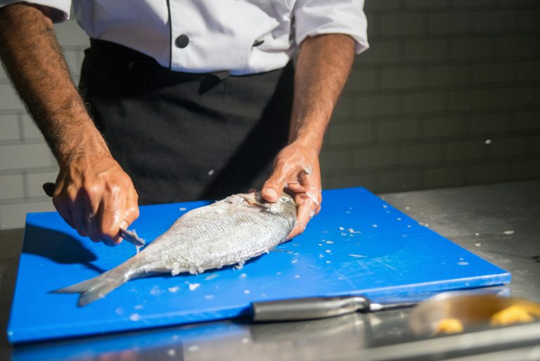 A person cleaning a raw fish on the cutting board