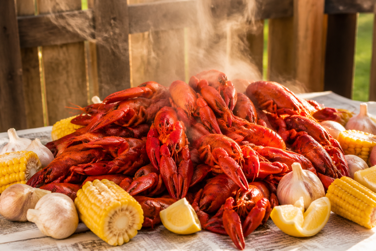 A massive pile of seasoned red boiled crawfish with corn and garlic on a newspaper-covered outdoor table