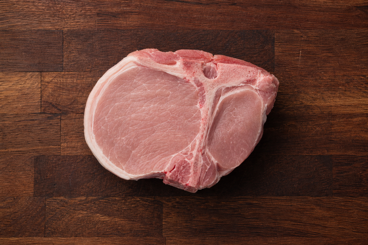 Raw center-cut loin pork chop with T-shaped bone on wooden cutting board