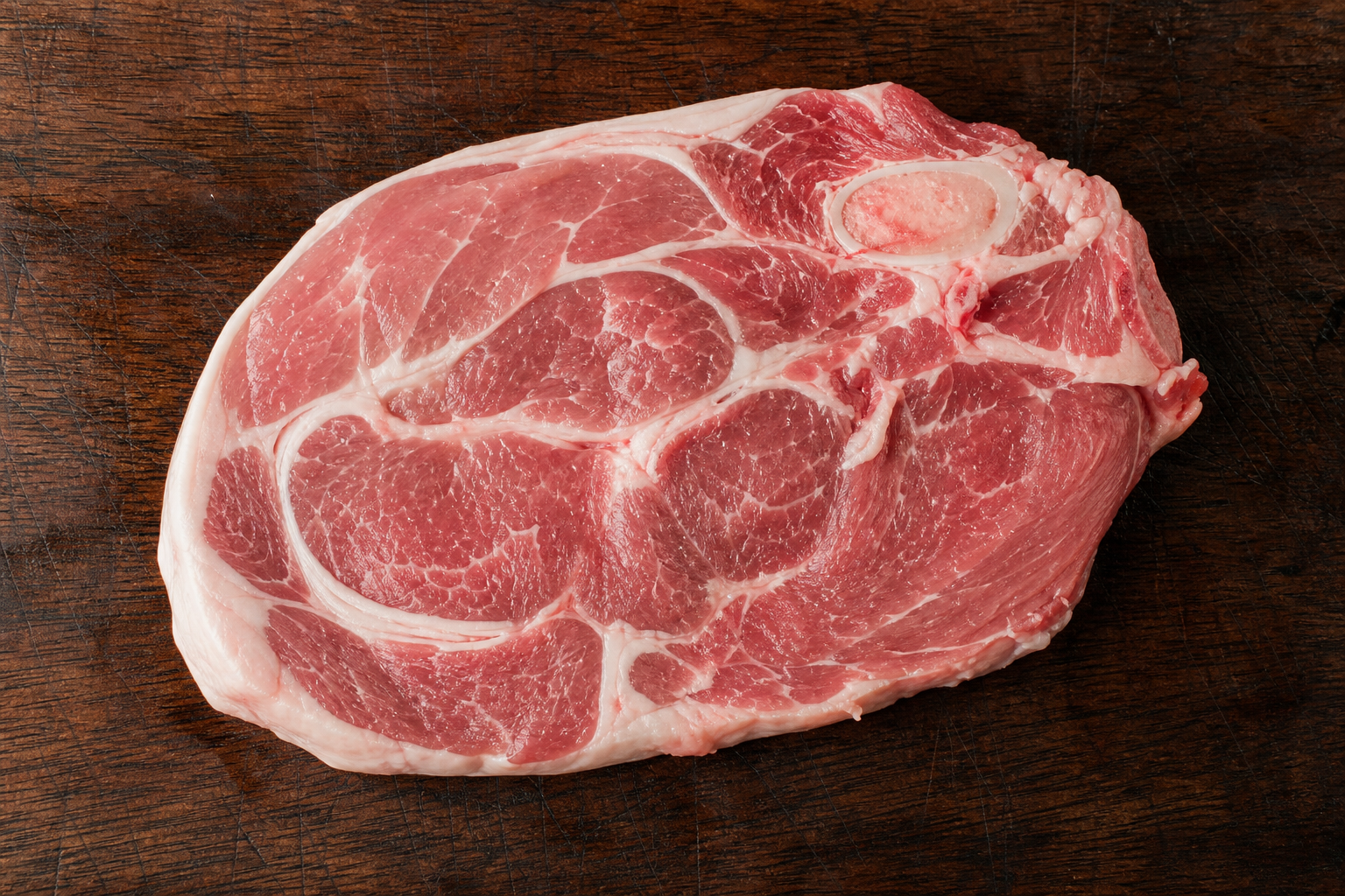 Raw bone-in pork shoulder steak on a wooden butcher block showing marbling and fat